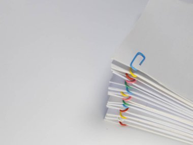 Renkli ataçlarla tutturulmuş beyaz kağıt çarşaf yığınını gösteren yakın plan bir fotoğraf. Resim, belge düzenlemek için kullanılan farklı renkli klipleri vurgulayarak, belgelerin organize düzenlenmesine odaklanır. Kompozisyon c