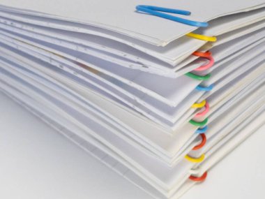 Yakın plan çekimlerde çeşitli renkli ataçlarla bir araya getirilmiş beyaz kağıt yığınları sergilenir. Kağıtlar, belgelerin düzenlenmesine görsel ilgi ve yardım sağlıyor. Görüntü, yumuşak ve doğal ışıklandırmayla bir stüdyo ortamında çekiliyor. Bu...