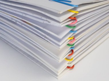 Renkli ataçlarla birbirine tutturulmuş bir yığın beyaz kağıt dökümanının yakın plan çekimi. Kağıtlar kırmızı, turuncu, sarı, yeşil, mavi ve pembedir. Görüntü, kağıt ve kliplerin kenarlarına odaklanan sığ bir alan derinliğine sahip. Bu... 