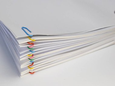 Renkli ataçlarla tutturulmuş beyaz kağıt yığınının yakın plan görüntüsü. Kağıtlar, tek tek çarşafları ve kliplerin canlı renklerini sergiliyor. Görüntü, organizasyonu ve evrak işlerini iletir.,