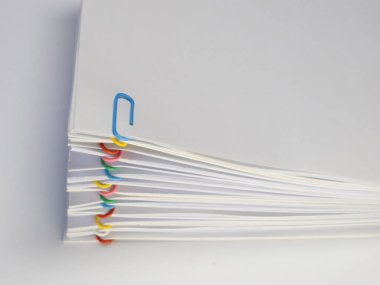 Renkli ataçlarla tutturulmuş beyaz kağıt yığınının yakın plan çekimi. Ataçlar farklı renklerde. Kağıtlar yayılıyor, bir organizasyon ya da kategorizasyon duygusu yaratıyor. Görüntü beyaz bir arkaplanda çekiliyor, ışıklandırma.