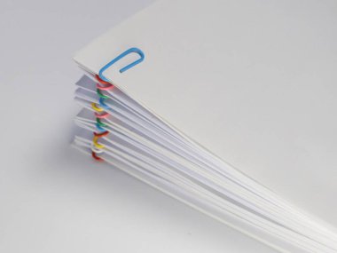 Çeşitli renkli ataçlarla tutturulmuş beyaz kağıtların yakın plan çekimi. Kağıtlar hafifçe yayılıyor, düzen ve düzen duygusu yaratıyor. Görüntü iyi aydınlatılmış, beyaz kağıt ve ataçları sergiliyor.. 