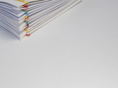 Çeşitli renkli ataçlarla tutturulmuş beyaz kağıt yığınının yakın plan fotoğrafı. Kağıtlar beyaz bir yüzeye istiflenmiş, temiz ve düzenli bir görünüm yaratıyor. Resim beyaz kağıt ve vibr arasındaki karşıtlığı vurgular