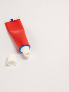 Beyaz arka planda kapağı olan açık kırmızı bir merhem tüpü. Tüpü sıkıyor ve küçük bir miktar merhem görünür durumda. Görüntü ışıl ışıl ve arka plan bembeyaz. Bu iğne tıbbi ve hoyrat için ideal.