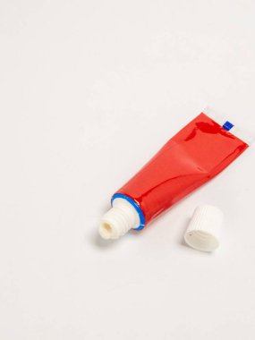 Bir stüdyo çekiminde kırmızı bir ürün tübü bulunur, muhtemelen beyaz bir yüzeye yerleştirilmiş merhem ya da boya. Kapak tüpten ayrılmış. Kompozisyon basit, nesne ve rengine odaklı. Resim iyi aydınlatılmış, metni vurguluyor