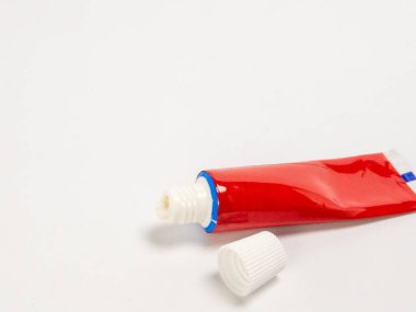 Sade beyaz bir yüzey üzerinde duran canlı kırmızı bir merhem tüpünün yakın plan çekimi. Kapak kapalı, içerideki ürünü ortaya çıkarıyor. Kompozisyon basit, temiz ve iyi aydınlatılmış. Tıbbi, kozmetik ya da ürünlerle ilgili çok yönlü bir görüntü. 