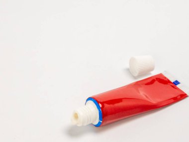 Açık kırmızı bir tüpün yakın plan görüntüsü, yanında da beyaz bir kapak var. Tüp temiz beyaz bir yüzey üzerinde duruyor. Tüp kapağının açılışı ve kapağı çok keskin, arka plan hafifçe bulanık. Görüntü, sağlık arabası gibi kavramları akla getiriyor.