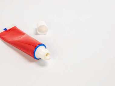 Kısmen kullanılmış bir kırmızı merhem tüpünün kapağı açık beyaz bir yüzeyde duran yakın plan görüntüsü. Tüpü sıkıyor ve az miktarda krem görünüyor. Kapak tüpün yanına yerleştirildi. Aydınlatma parlak ve eşit, vurgu