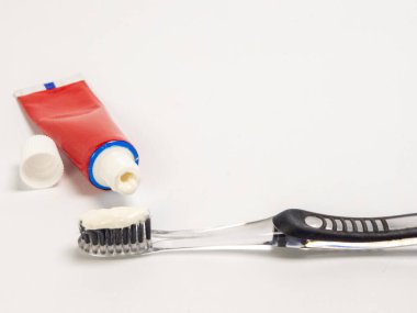 Temiz bir diş fırçasının yanına yerleştirilmiş kapağı açık kırmızı bir diş macunu tüpünün yakın plan çekimi. Diş macunu kullanıma hazır bir şekilde kılların üzerine sıkışıyor. Resim temiz, beyaz bir arkaplana göre ayarlanır, oral odak noktası vurgulanır