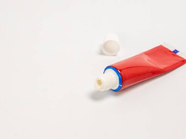 Yakın plan bir stüdyo çekiminde yanında beyaz şapkası olan kırmızı bir merhem tüpü görülüyor. Tüp temiz, beyaz bir zemin üzerinde duruyor ve bazı merhemler açılışta görülebilir. Görüntünün iyi bir ışıklandırması ve nötr bir tonu var.