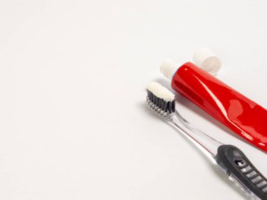 Kırmızı bir diş macunu tüpü, açık beyaz bir kapak ve beyaz bir yüzey üzerinde siyah tüyleri olan temiz bir diş fırçası. Diş fırçasının kıllarına beyaz diş macunu uygulanır. Kompozisyon basit, temiz ve diş hijyenine odaklı.