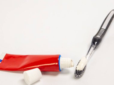 Kırmızı bir diş macunu tüpü ve diş fırçasının tüylerinde diş macunu olan temiz beyaz bir arkaplan ile yakın plan çekimi. Kompozisyon, nesnelerin detaylarına ve mağara kavramına odaklanarak, temel ağız temizliği öğelerini vurgular.