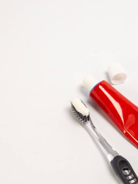 Diş macunlu bir diş fırçası ve beyaz bir yüzeye karşı kırmızı bir diş macunu tüpü ile yakın plan bir çekim. Temiz diş fırçası siyah tüylere sahiptir ve bol miktarda diş macunu görülebilir. Kırmızı tüp kısmen görülebilir.