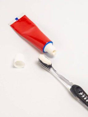 Diş fırçasının beyaz diş macunuyla yakından çekilmiş bir fotoğrafı, diş fırçasının yanında kırmızı bir tüp var. Kapağı çıkarıldı. Sahne sade beyaz bir arkaplanda, temiz ve minimalist bir kompozisyon yaratıyor. Görüntü e 'yi yakalar.