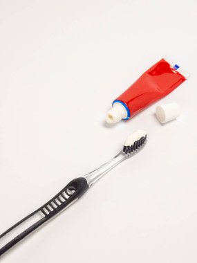 Diş fırçası, diş macunu ve kırmızı tüp ile yakın plan görüntüsü, düz beyaz bir arkaplanda izole edilmiş. Diş fırçası kısmen beyaz diş macunuyla kaplıdır. Kırmızı diş macunu tüpü kapağı yanında açık. Görüntü iyi ışıklandırılmış.