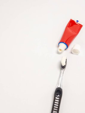 Tepeden çekimde siyah ve temiz bir diş fırçası, diş macunu ve kapaklı kırmızı bir diş macunu bulunur. Nesneler temiz ve beyaz bir arkaplana göre ayarlanmış. Bu resim, diş sağlığı için ideal olan kişisel hijyen ve günlük rutini vurgular.