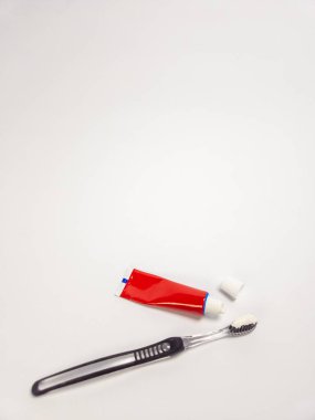 Beyaz diş macunu, kırmızı diş macunu tüpü ve beyaz arka planda kapağı olan siyah bir diş fırçasının yakın plan fotoğrafı. Görüntü iyi aydınlatılmış, diş temizliği araçlarının temizliğini ve basitliğini vurguluyor. Kompozisyon gayet açık.