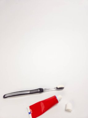 Yakın plan çekimde siyah diş fırçası, beyaz diş macunu ve kapağı çıkarılmış kırmızı bir diş macunu bulunur. Ögeler düz beyaz bir arkaplanda düzenlenmiştir. Odaklanma, ağız hijyeninin basitliği ve gerekliliklerine odaklanmaktır.