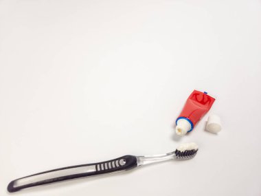 Diş macunlu bir diş fırçası ve beyaz arka planda kırmızı bir diş macunu tüpü. Diş fırçası siyah ve temizdir ve diş macunu beyazdır. Tüpü beyaz şapkalı kırmızı. Görüntü basit ve temiz, objelere odaklı..