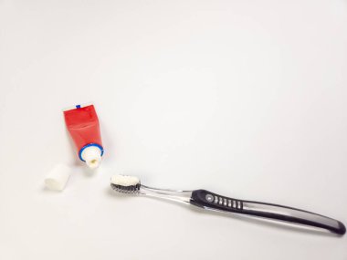 Yakın çekim, diş macunu sürmüş bir diş fırçasını, açık bir diş macunu tüpü ve kapağının yanında, düz beyaz bir yüzey üzerine yerleştirilmiş bir şekilde yakalar. Bu resim, ağız temizliğine odaklanmış basit ve temiz bir kompozisyon sunuyor, de için mükemmel.