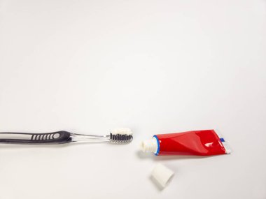 Diş macunlu temiz bir diş fırçası ve kapağı açık kırmızı bir tüp, düz beyaz bir yüzeye yerleştirilmiş. Kompozisyon basit ve temiz. Ağız hijyeninin temel unsurlarını vurguluyor. Görüntü bir temizlik ve tazelik hissi veriyor.