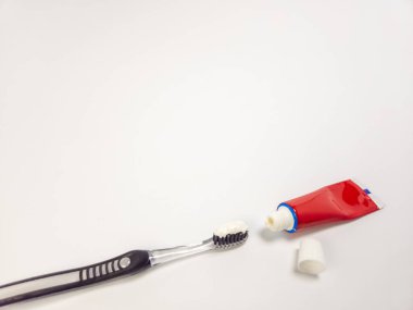 Diş macunu sürmüş bir diş fırçasının yakın çekimi, yanında açık bir diş macunu tüpü ve kapağı var. Görüntü, ağız hijyeni ve diş bakımına odaklanmayı vurgulayan temiz, beyaz bir arkaplan üzerine kurulmuştur. Kompozisyon basit ve temiz.,