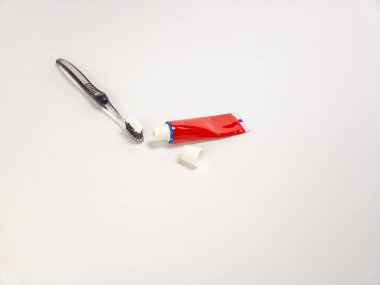 Diş fırçasının beyaz diş macunuyla yakın plan fotoğrafı, ve kırmızı beyaz diş macunu tüpü, artı beyaz arka plan kapağı. Görüntü iyi aydınlatılmış ve ağız hijyeninin temel unsurlarını gösteriyor. Odaklan.