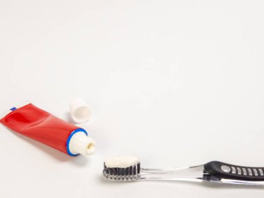 Kapağı açık kırmızı bir diş macunu tüpü, yanında siyah ve gümüş diş fırçası ve diş macunu. Sahne, temiz ve beyaz bir arka plana göre ayarlanmış. Bu da diş hijyenine odaklandığını gösteriyor. Görüntü iyi aydınlatılmış ve açıkça bunu gösteriyor.