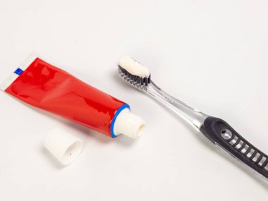 Kırmızı bir diş macunu tüpü ve diş fırçasının beyaz bir arka planda diş macunu ile yakın plan çekimi. Kompozisyon basit, diş bakımı için gerekli araçları vurguluyor. Görüntü, temiz ve taze görünüşü sergiliyor.