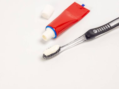 Diş fırçasının yakından çekilmiş bir fotoğrafı, diş macunu kılların üzerine sıkılmış, kırmızı diş macunu tüpünün yanında, kapağı kapalı. Temiz diş fırçası sapı ve beyaz arka plan temiz ve basit bir kompozisyon oluşturuyor. Bu resim ağız hijyenini temsil ediyor.