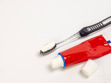 Diş fırçasıyla diş macunu ve beyaz arka planda bir tüp diş macunu. Kırmızı tüp açık, yanında da kapağı var. Diş fırçası kılların üzerinde diş macunu ile açılıdır. Görüntü temizliği ve diş temizliğini iletir.