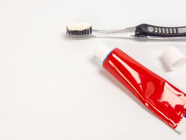 Üzerinde diş macunu olan bir diş fırçası ve beyaz bir yüzeyde duran kapağı çıkarılmış kırmızı bir diş macunu tüpü. Kompozisyon temiz ve basit, iyi ışıklandırmayla. Görüntü diş bakımı, ağız sağlığı ve sağlık için uygundur., 