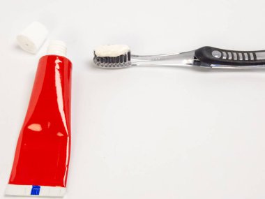 Kapağı açık kırmızı bir diş macunu tüpünü, diş fırçasının yanında diş macunu lekesi olan yakın plan bir fotoğraf. Ögeler düz beyaz bir zemine yerleştiriliyor, temiz ve basit bir kompozisyon oluşturuyor. Bu resim vurgular 