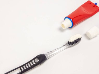 Tepeden tırnağa görüntülerde diş macunu sürmüş bir diş fırçası, kırmızı bir diş macunu tüpü ve kapağının yanında, hepsi temiz beyaz bir arkaplan üzerine kurulmuş. Görüntü ağız temizliği, diş bakımı ve diş fırçalamanın günlük rutinini vurguluyor.