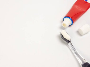 Siyah tüylü, temiz bir diş fırçasının yakın çekimi ve yanında da kapaklı bir tüp kırmızı diş macunu. Bir tutam beyaz diş macunu fırçanın üzerinde kullanıma hazır. Sahne, temiz beyaz bir arkaplan üzerine kurulmuştur. Bu resim mağara için mükemmel.