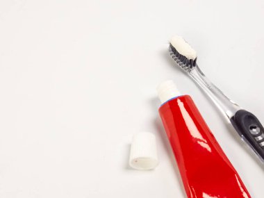 Diş fırçasının, diş macununun kapağı açık kırmızı bir diş macununun yanında yakın plan fotoğrafı. Eşyalar beyaz bir yüzeyde düzenlenir ve kompozisyon basit ve temizdir, diş hijyeni veya sağlık teması için mükemmeldir. T