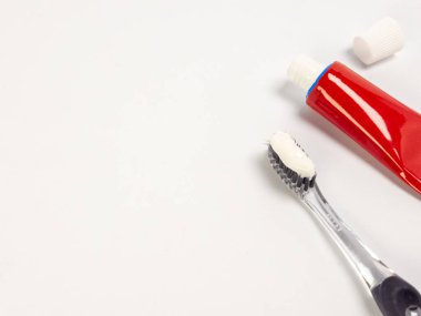 Diş fırçası, diş macunu ve açık bir tüp. Diş fırçası sağ tarafa yerleştiriliyor, yanında da diş macunu tüpü var. Arka plan bembeyaz, temiz ve minimalist bir estetik oluşturuyor. Görüntü iyi aydınlatılmış.
