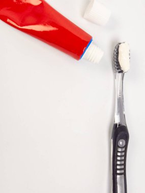 Yakın plan bir stüdyo çekiminde, kapağı çıkarılmış kırmızı diş macunu tüpünün yanında diş macunu olan siyah bir diş fırçası görülüyor. Eşyalar düz beyaz bir yüzeye yerleştirilmiş. Bu da diş bakımı ve kişisel hijyene odaklandığını gösteriyor. Görüntü biziz.