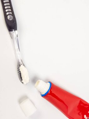 Diş fırçasının diş fırçasının, diş fırçasının diş fırçasına sürtünmesi ve açık bir diş macunu tüpü ve kapağı. Nesneler, diş sağlığı ve ağız hijyenine odaklanarak temiz beyaz bir arkaplan üzerine kurulmuştur. Canlı kırmızı küvet.