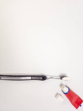 Diş macununa sürülen siyah ve berrak bir diş fırçasının yakın plan bir fotoğrafı, yanında da kapağı çıkarılmış kırmızı bir diş macunu tüpü. Eşyalar temiz beyaz bir arka plana yerleştiriliyor, diş bakımı, hijyen ve hoyrat için uygun.