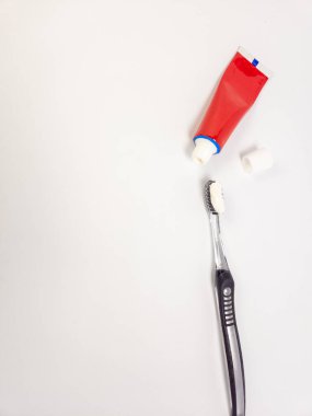 Diş fırçasının tepesinde bir diş macunu ve yanında da kırmızı bir diş macunu tüpü. Eşyalar, diş bakımı ve ağız hijyenini vurgulayarak temiz, beyaz bir arkaplanda düzenlenir. Görüntü iyi aydınlatılmış, odaklanılmış. 