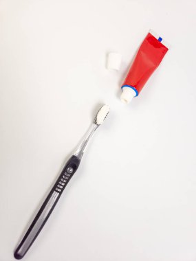 Bir üstten çekimde siyah ve gümüş diş fırçası ve diş macunu kullanılıyor, yanında da kapağı çıkarılmış kırmızı bir diş macunu tüpü var. Görüntü, diş bakımını ve ağız temizliğini vurgulayan temiz, beyaz bir arka plana göre ayarlanmış. Kompozisyon I