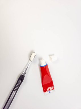 Yakın plan, tepeden çekimde diş macunu sürülmüş siyah ve gümüş bir diş fırçası ve kısmen sıkılmış kırmızı bir diş macunu tüpü ile kapağı çıkarılır. Eşyalar düz beyaz bir yüzeye yerleştiriliyor. Görüntü çöküntü konseptini iletir