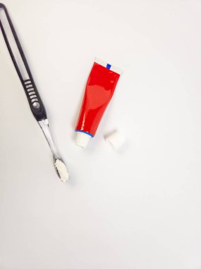 Yukarıdan aşağıya bakıldığında diş macunlu bir diş fırçası, açık kırmızı bir diş macunu tüpü ve kapağı el değmemiş beyaz bir fonda görülüyor. Görüntü diş hijyenini minimalist ve temiz estetikle ön plana çıkarıyor. Kompozisyon basit, t 'ye odaklanıyor.