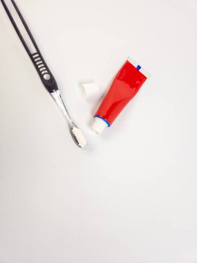 Kapağı açık kırmızı bir diş macunu tüpünün yanında diş macunlu siyah bir diş fırçasını gösteren natürmort. Nesneler temiz, parlak beyaz bir yüzeye yerleştirilirler ve basit ve minimalist bir kompozisyon oluştururlar. Resim boşalt