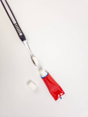 Bir stüdyo çekimi, diş fırçasını kıllarında diş macunuyla yakalar ve kapağı açık kırmızı bir diş macunu tüpü, hepsi de el değmemiş beyaz bir zemine dayanır. Kompozisyon basit ve temiz, ağız hijyeninin temel unsurlarını vurguluyor. Th