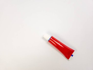 Kırmızı bir krem ya da merhem içeren bir stüdyo çekimi, düz beyaz arka plana çapraz yerleştirilmiş. Tüp, beyaz şapkası, mavi aksanlı şeridi ve beyaz uçlu başlığı ile birincil denek. Işıklandırma yumuşak, tüpün gl 'ını vurguluyor.