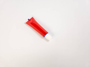 Kırmızı bir krem tüpünün yakın çekim stüdyosu, muhtemelen tıbbi kullanım için, beyaz arka planda köşegen olarak dinleniyor. Tüpün beyaz ve mavi bir aksanı var. Bu da cilt bakımı ya da sağlık ürünleri olduğunu gösteriyor. Geniş kopya alanı olan temiz kompozisyon, suit abl