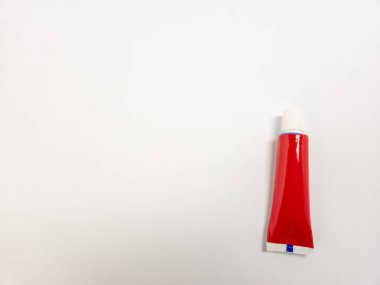 Kırmızı bir merhem ya da krem tüpünün beyaz bir arka plana yakın çekim çekimi. Tüpün sonunda beyaz bir kapak ve mavi bir şerit vardır. Görüntü iyi aydınlatılmış, tüpün üzerine odaklanmış. Arka plan temiz, ürünü vurguluyoruz..