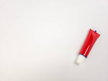 Beyaz arka planda parlak kırmızı bir tüpün yer aldığı yakın plan bir stüdyo çekimi. Tüp açılı, şeklini ve tasarımını gösteriyor. Ürünün rengini ve şeklini vurgulayan kompozisyon basittir. Bu resim kozmetik ürünleri için uygun, güzellik.